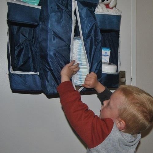 A toddler boy reaching the navy nursery organizer, opening the nappy pocket and looking at nappies.