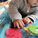 A baby lying on his tummy looking at the foam toys inside the sea-life water play mat.