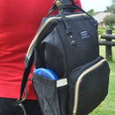 A lady walking with the black backpack nappy bag on her shoulder.
