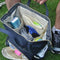 A backpack nappy bag open on the grass. It is filled with bum cream, clothes, wet wipes and other baby items