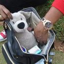 Hands reaching into a backpack nappy bag. It is filled with a plush dog, nappy cream and a baby bottle.