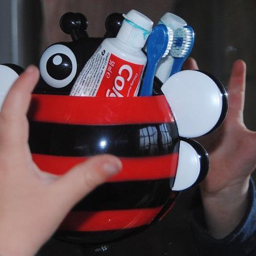Little hands holding a red bee toothbrush holder. There is a toothbrush and toothpaste inside the holder.